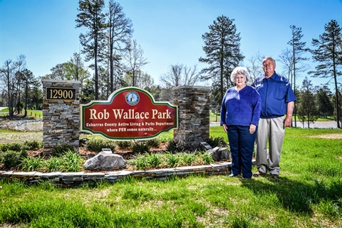 Mr. and Mrs. Wallace Standing Next To The Rob Wallace Park Sign