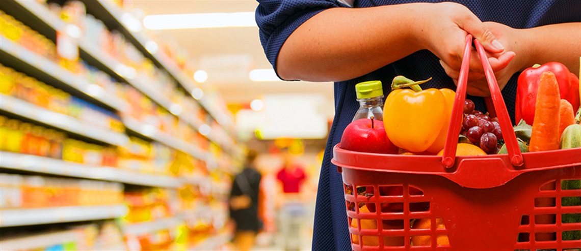 Person in Store Aisle Holding a Full Grocery Basket